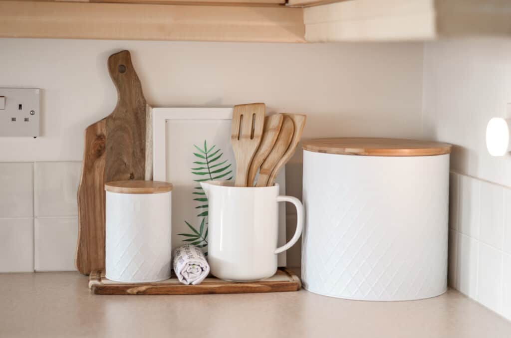 minimalist countertop with wooden spatulas, serving boards and white canisters